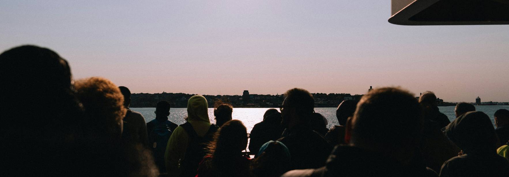 Una multitud de personas se encuentra en un barco mientras observan el mar al atardecer.