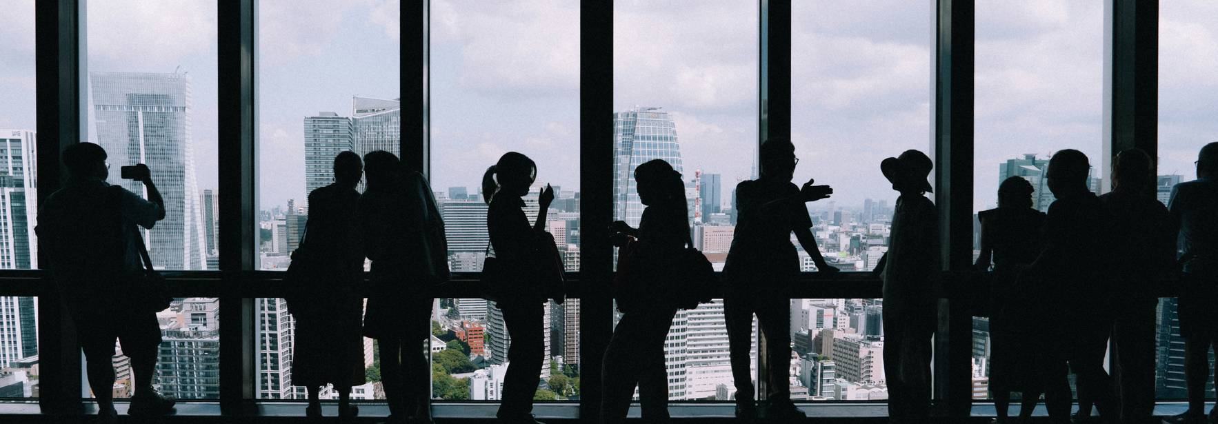 Silhouetas de personas observando la ciudad a través de una ventana grande.