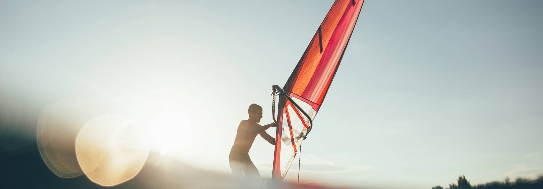 Un hombre navegando en una tabla de windsurf al atardecer.