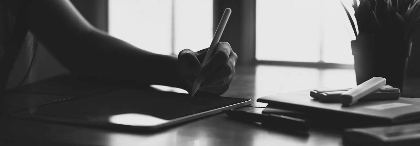 Una mano escribe en una tablet sobre una mesa con diversos objetos de oficina.