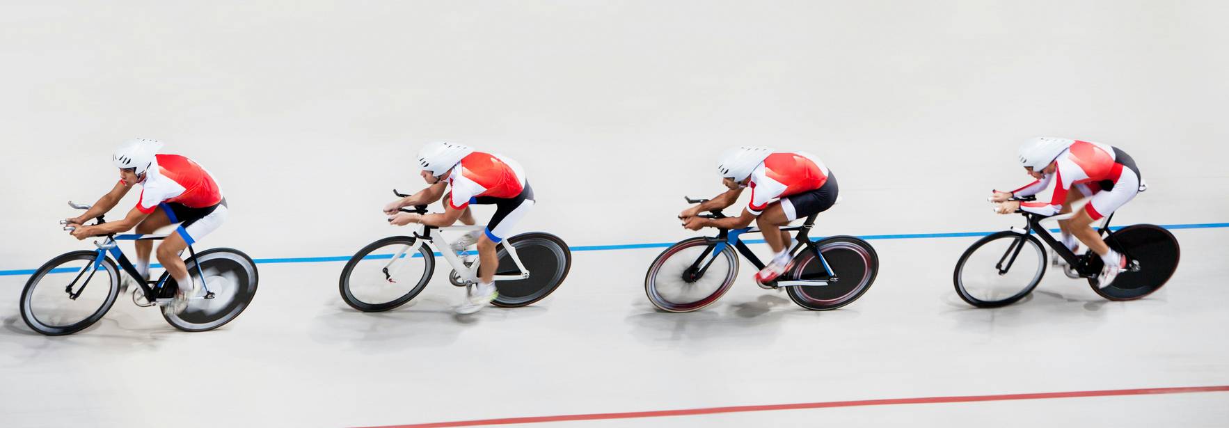 Cuatro ciclistas compiten en una pista de ciclismo de velocidad.