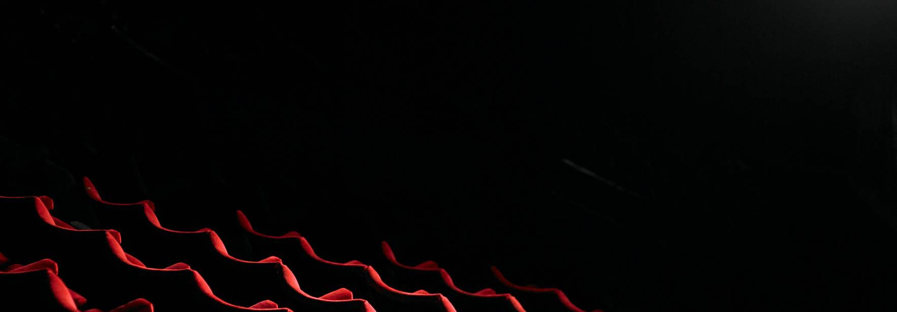 Una fila de asientos rojos en un teatro iluminada por una luz tenue.