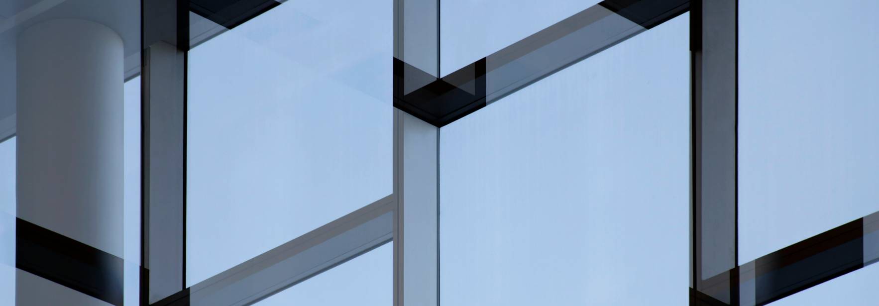 Una fachada moderna de vidrio con patrones geométricos y un cielo azul reflejado.