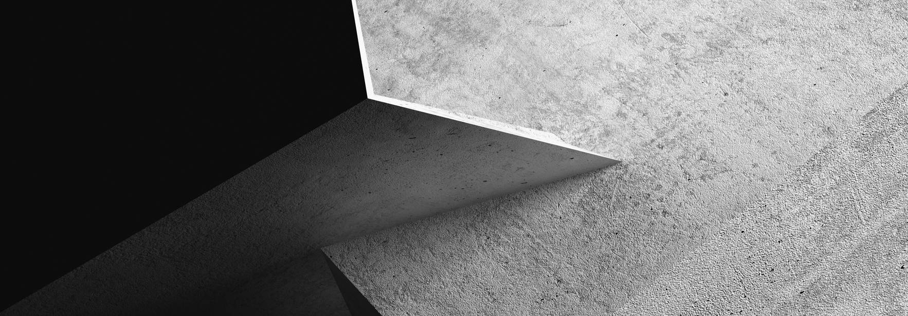 La imagen muestra una combinación de superficies de concreto en tonos grises, formando ángulos agudos y contrastes de luz y sombra.