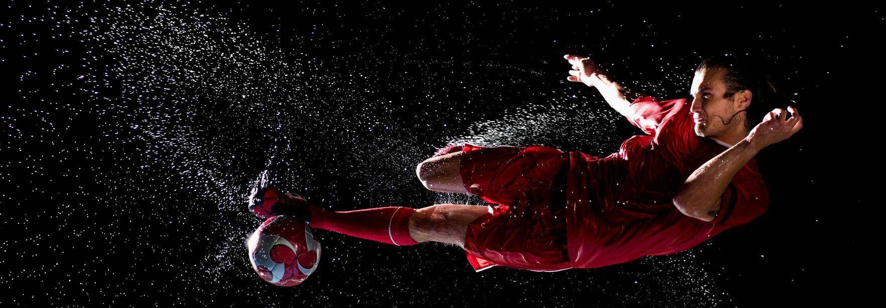 Un jugador de fútbol en acción realizando un tiro mientras el agua salpica a su alrededor.