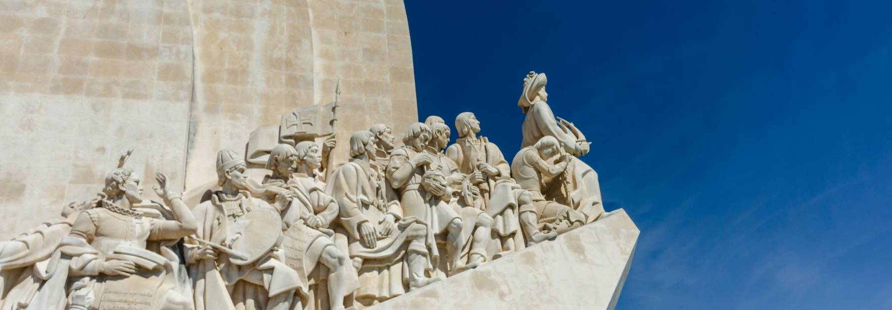 La imagen muestra un monumento con esculturas de figuras históricas en un fondo azul claro.