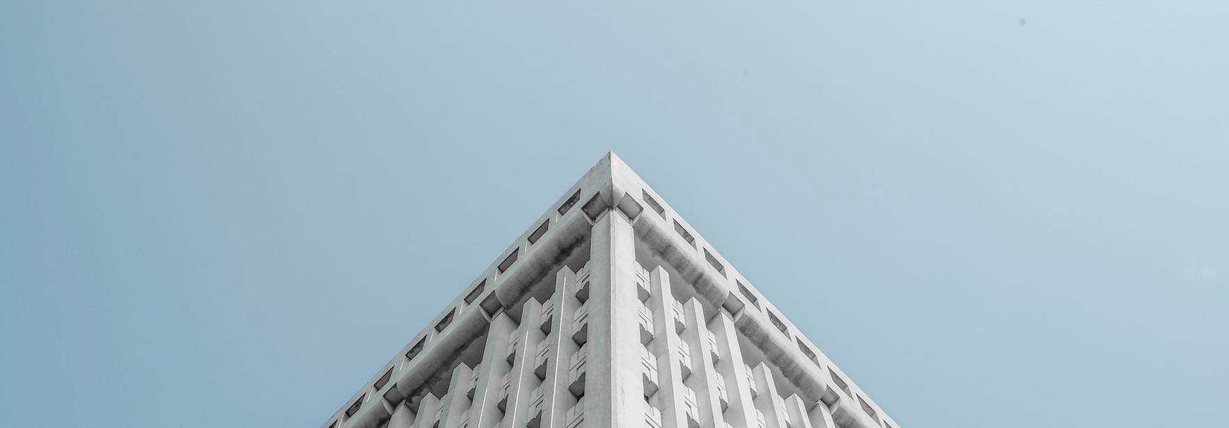 La imagen muestra la esquina superior de un edificio moderno contra un cielo claro.