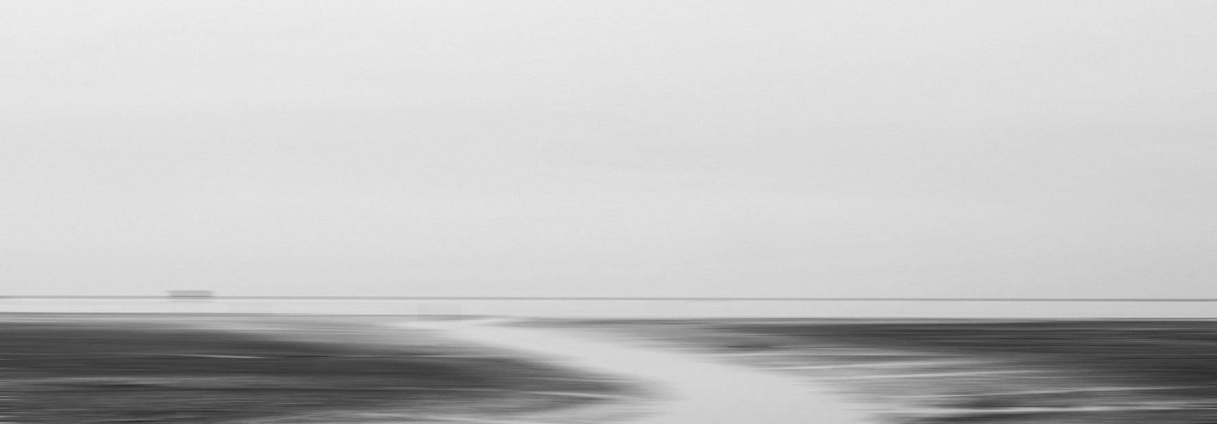Una escena minimalista en blanco y negro que muestra un paisaje costero con un camino de agua que se extiende hacia el horizonte.