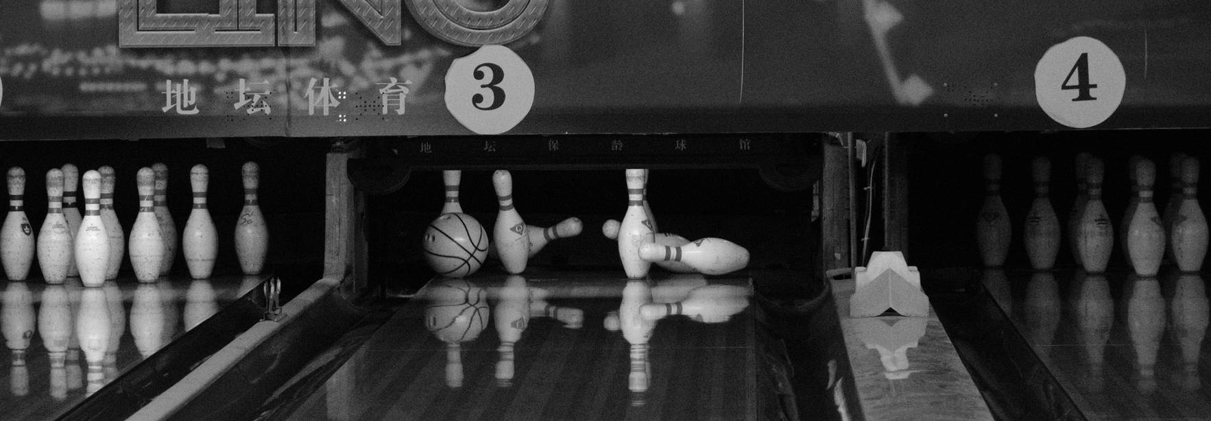 Una pista de boliche con pinos y una bola de boliche en el aire.