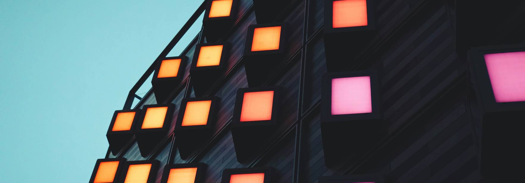 La imagen muestra un edificio moderno con luces de colores en sus fachadas.