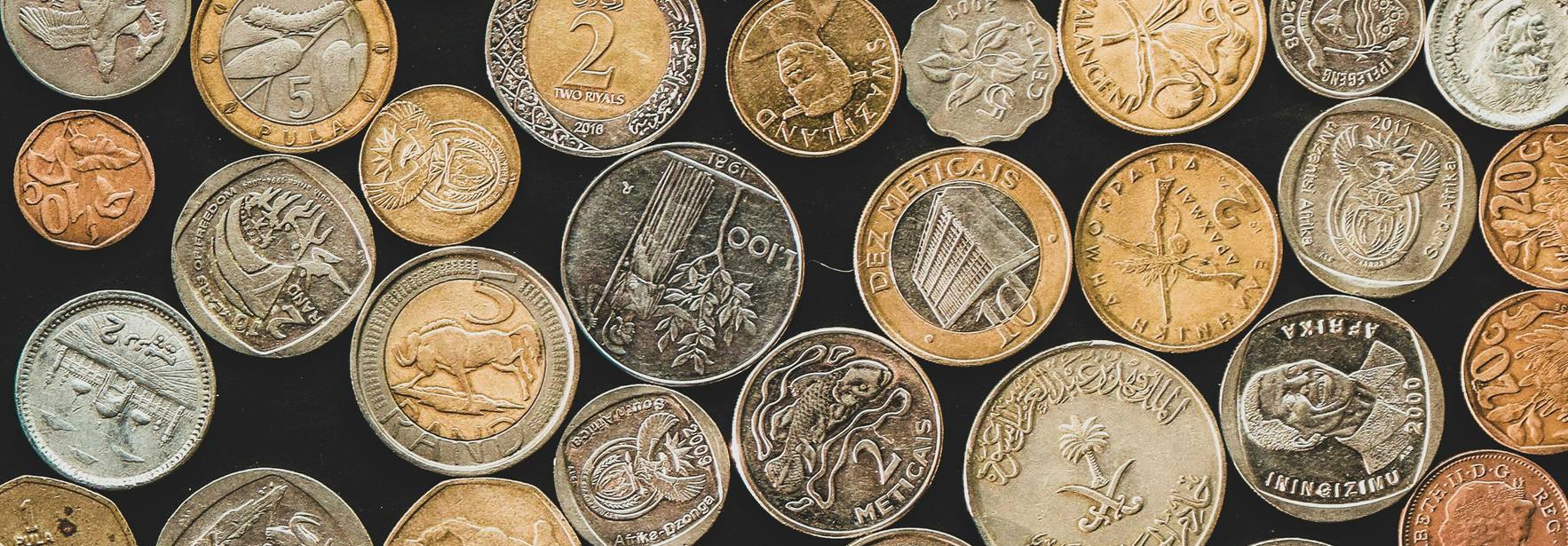 Una colección variada de monedas de diferentes tamaños y colores dispuestas sobre un fondo oscuro.