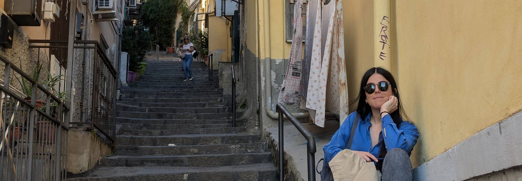Una persona sentada en las escaleras de una calle estrecha y soleada.