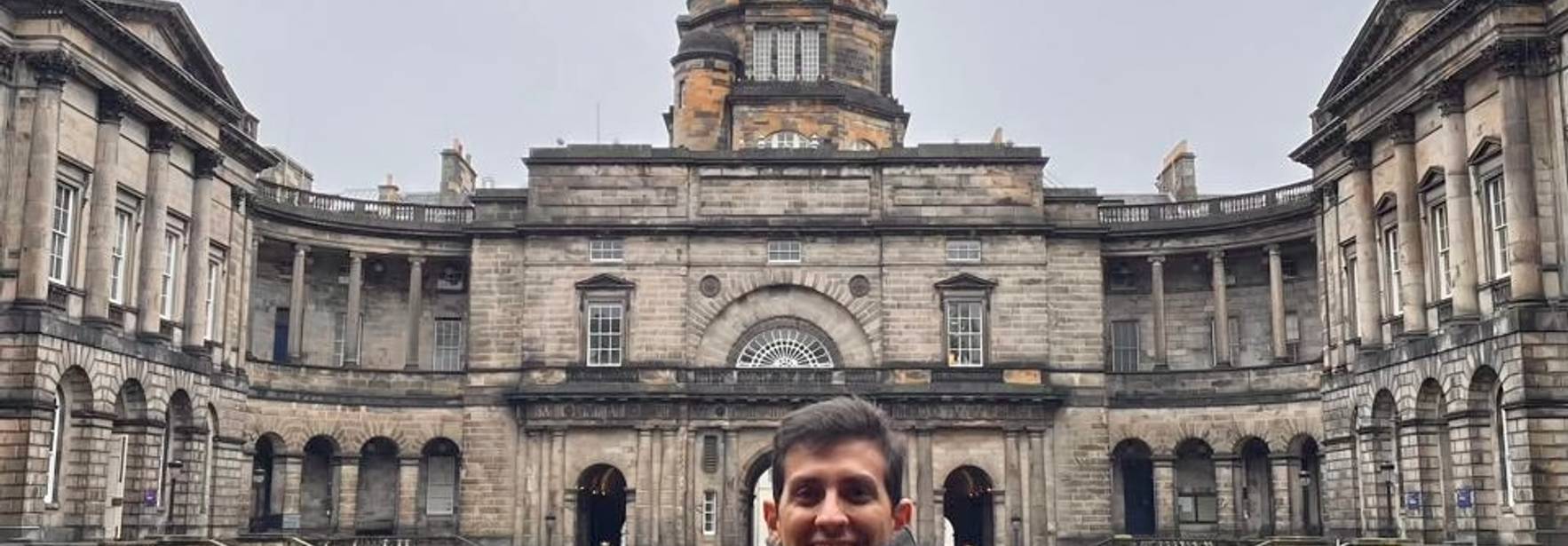 Un hombre de pie frente a un majestuoso edificio con cúpula en un día nublado.