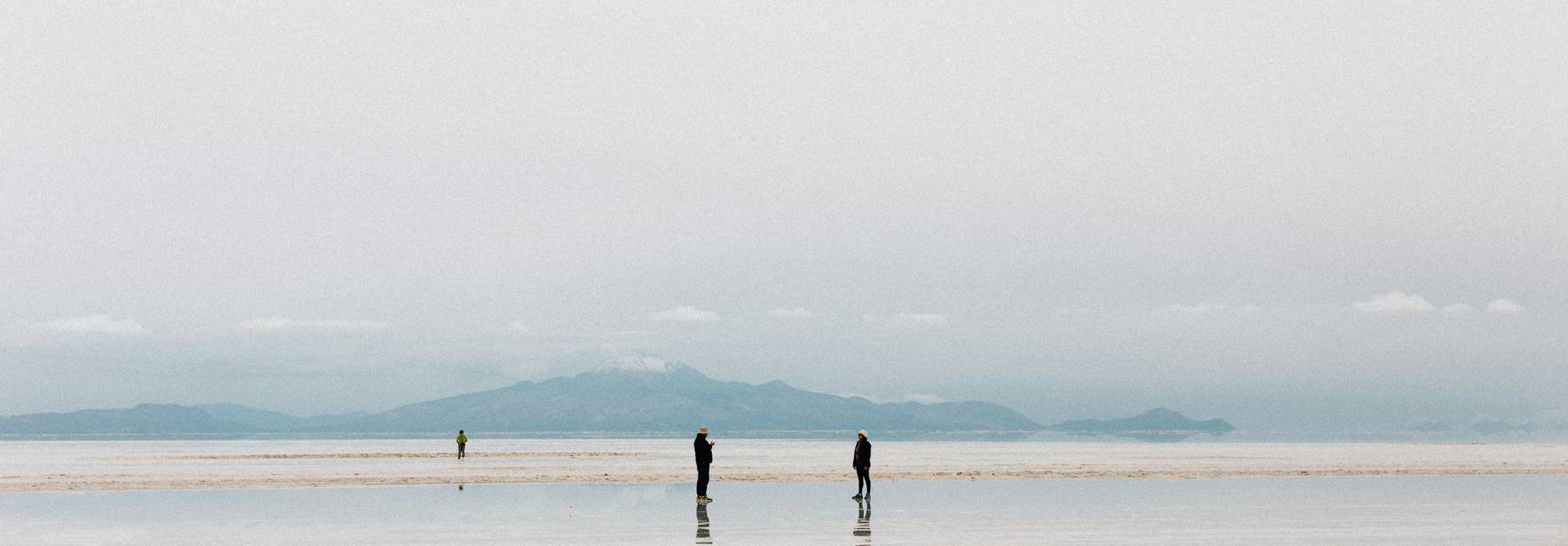 Dos personas caminan sobre una superficie reflectante en un paisaje natural sereno.