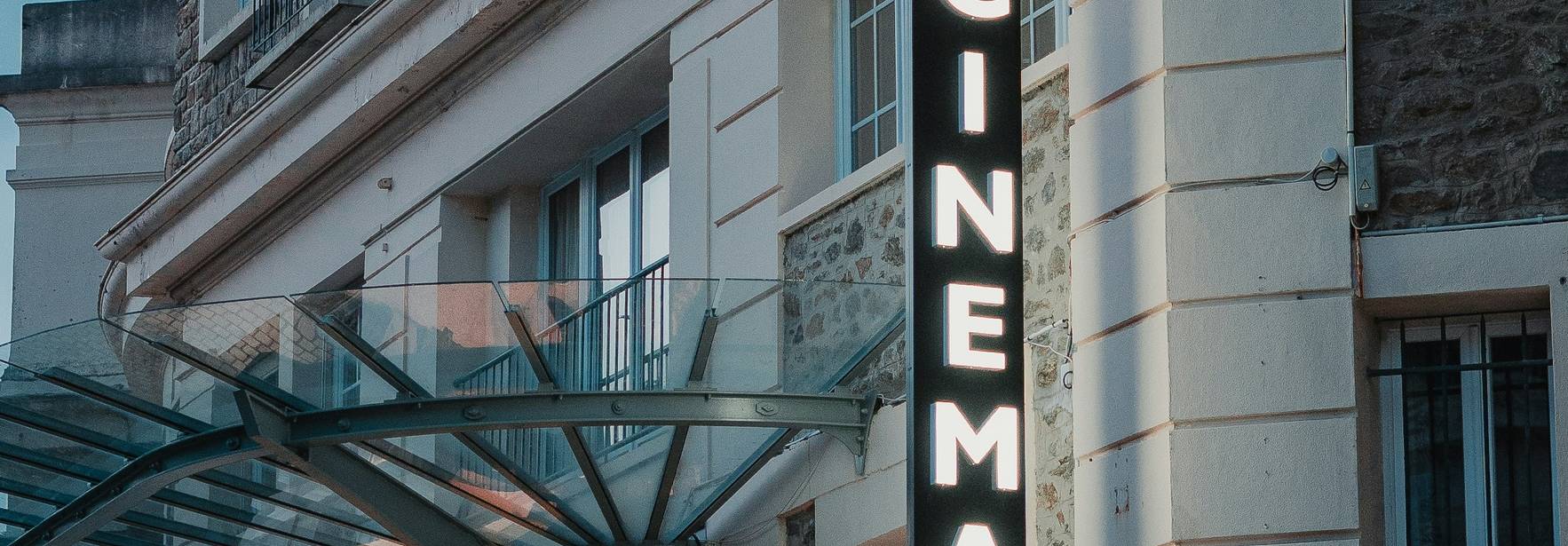 Fachada de un cine iluminada por letreros en una calle urbana.