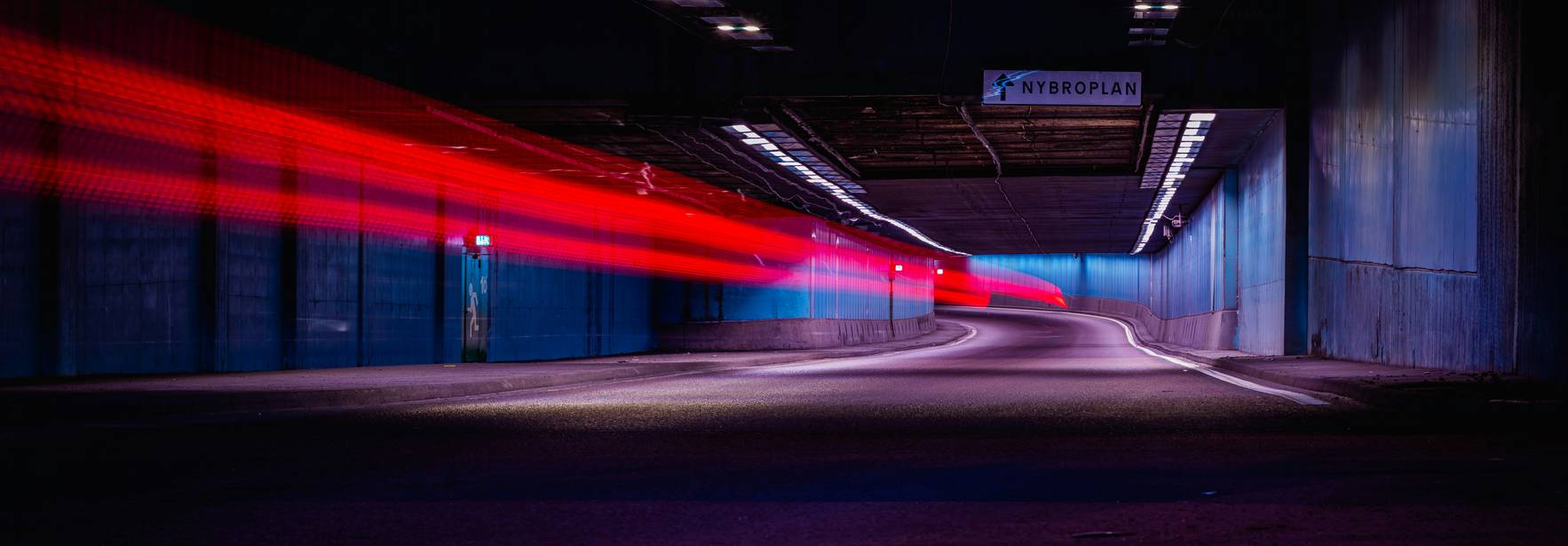 Una imagen de un túnel oscuro con luces rojas que se mueven rápidamente y paredes azuladas.