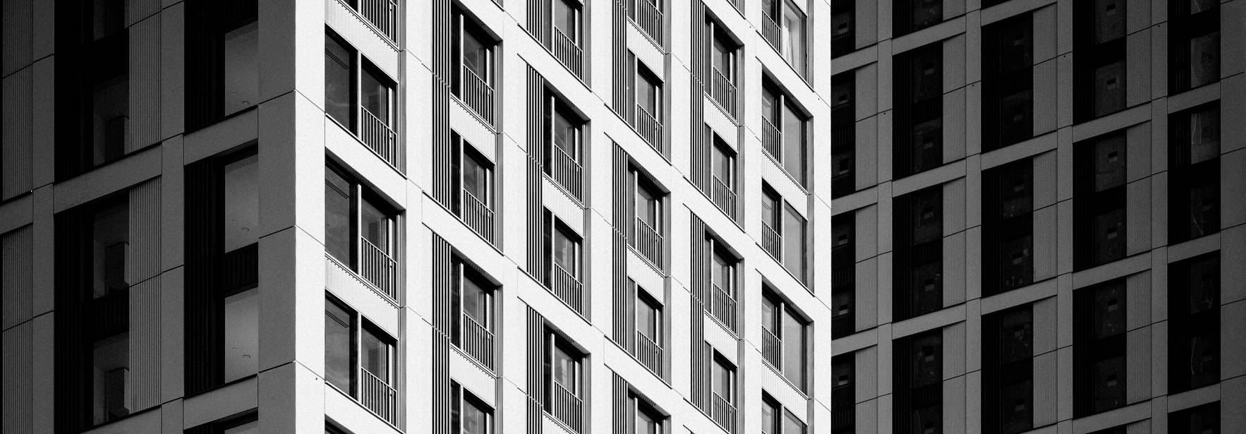 Imagen en blanco y negro que muestra la fachada de dos edificios con líneas geométricas y ventanas.