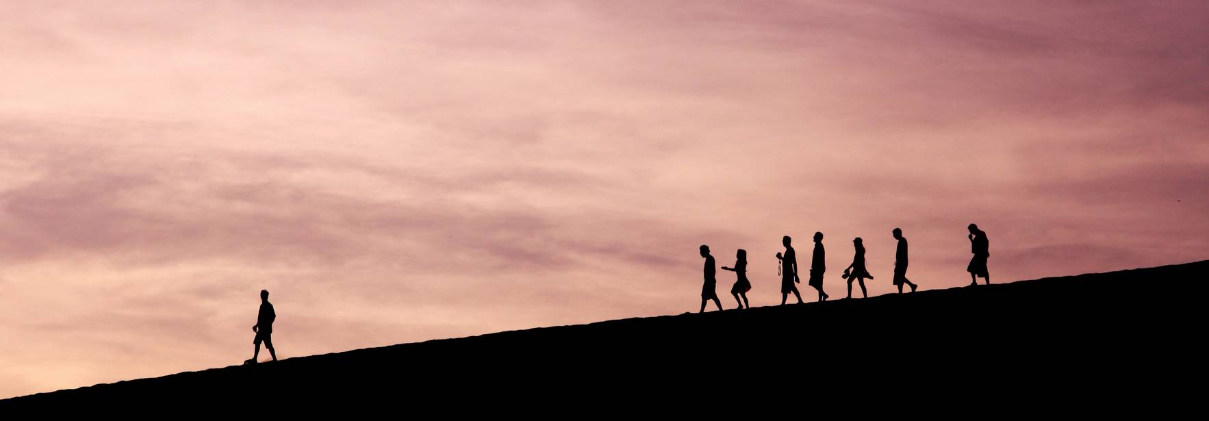 Grupos de personas caminando en una colina durante un atardecer.
