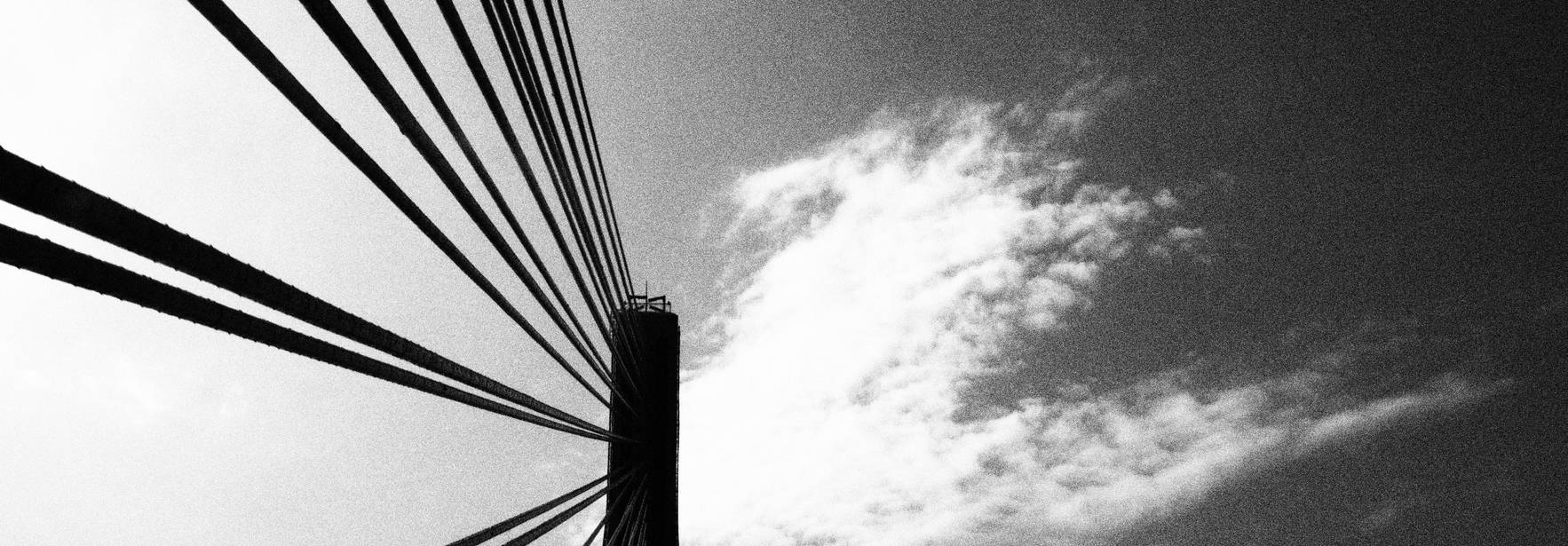 Una imagen en blanco y negro de un puente con cables tensados contra un cielo nublado.
