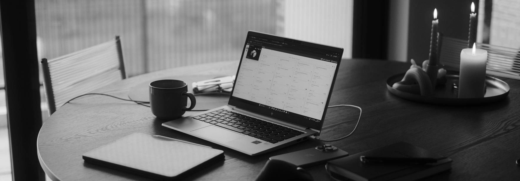 Una mesa de madera con un ordenador portátil, una taza de café, y velas encendidas.
