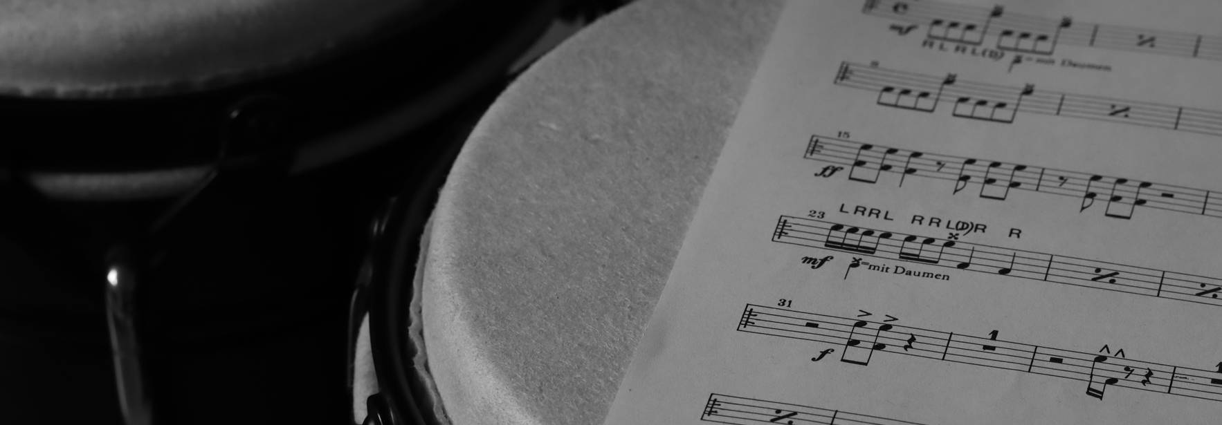 La imagen muestra un par de bongos junto a una partitura de música en blanco y negro.