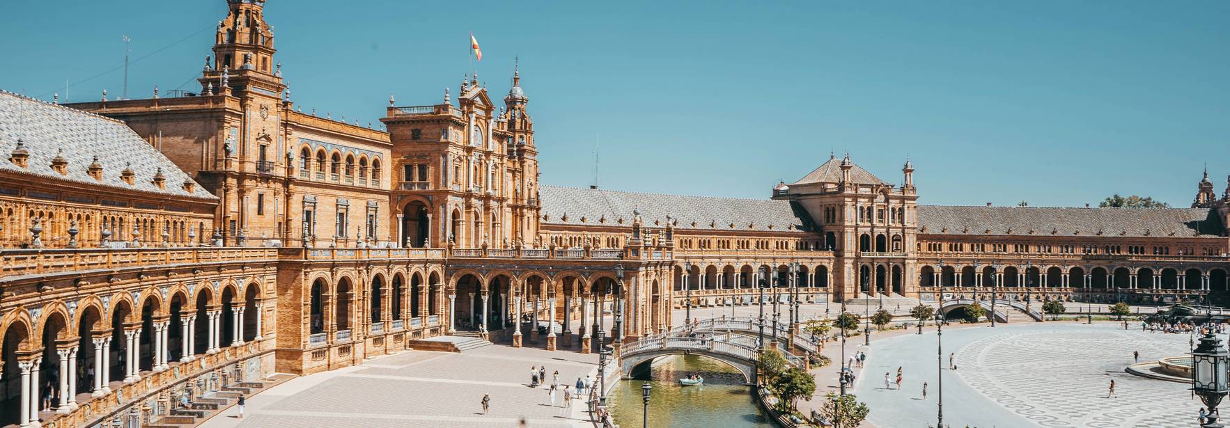 La imagen muestra la Plaza de España en Sevilla, un emblemático monumento innovador con arquitectura neomudéjar y un canal que la rodea.