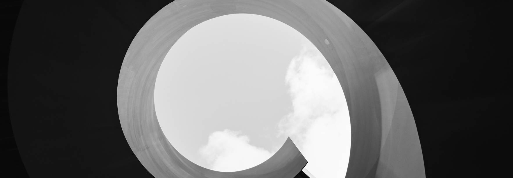La imagen muestra una espiral en blanco y negro con un cielo nublado al fondo.