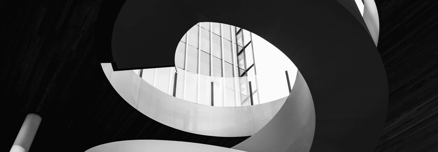 Una escalinata en espiral que se eleva hacia una estructura de vidrio en un entorno minimalista.