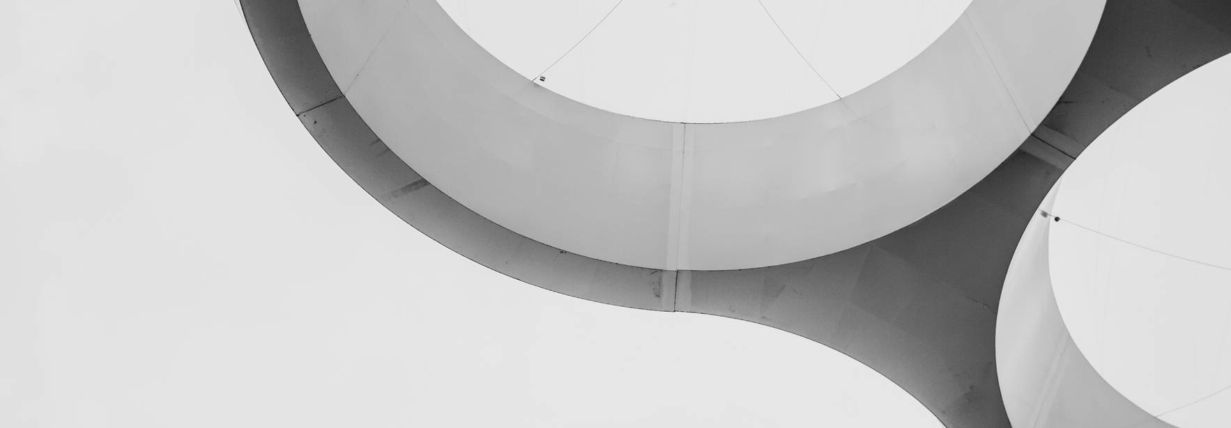 Una estructura arquitectónica moderna con formas circulares y líneas fluidas sobre un fondo nublado.