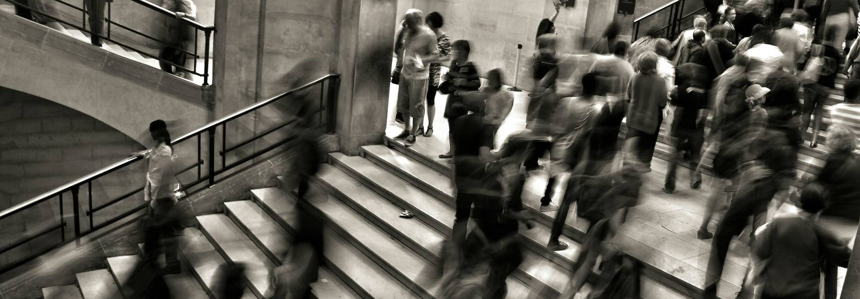 Una multitud de personas se mueve rápidamente por unas escaleras en un espacio arquitectónico moderno.