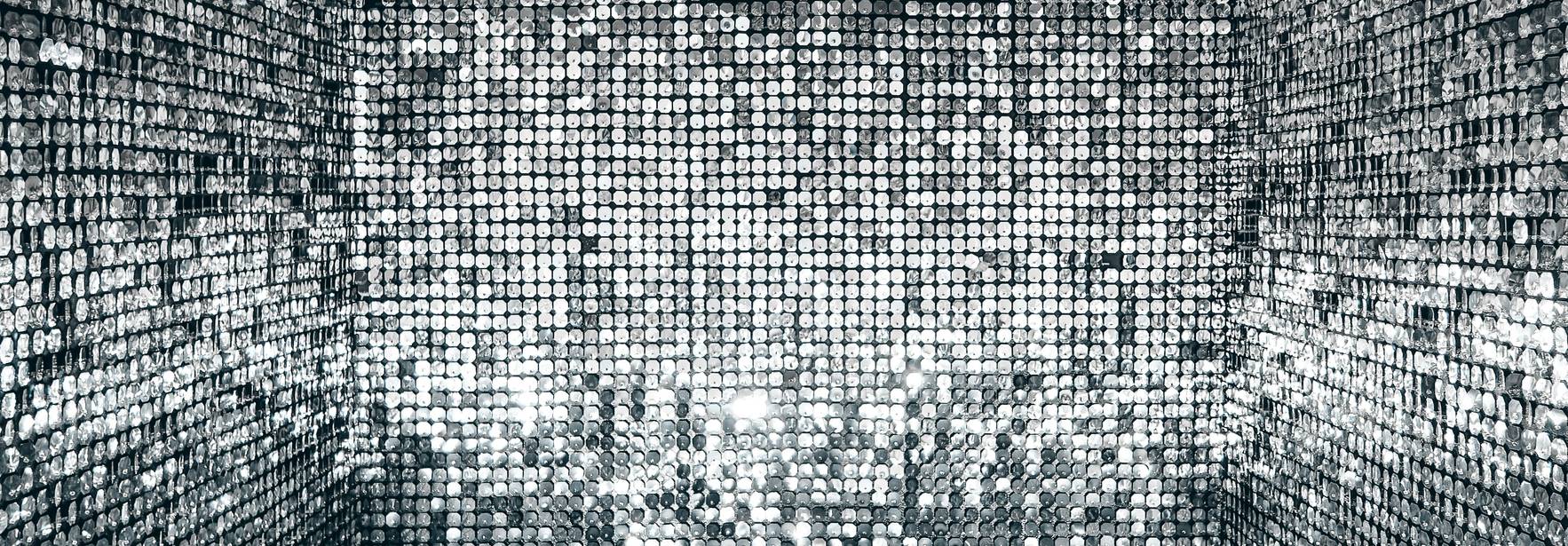 La imagen muestra un ambiente cubierto de superficies brillantes que reflejan luces en patrones deslumbrantes.