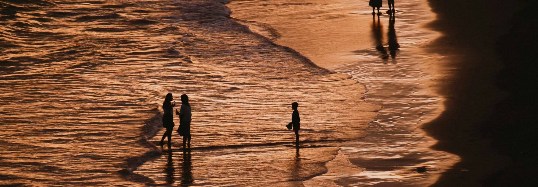 Una hermosa escena en la playa durante el atardecer, donde se pueden ver siluetas de personas disfrutando del mar.