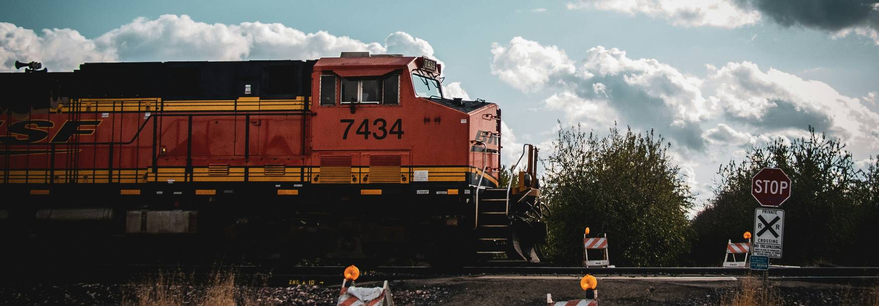 Un tren de carga rojo pasa por una vía con señales de stop y barricadas.