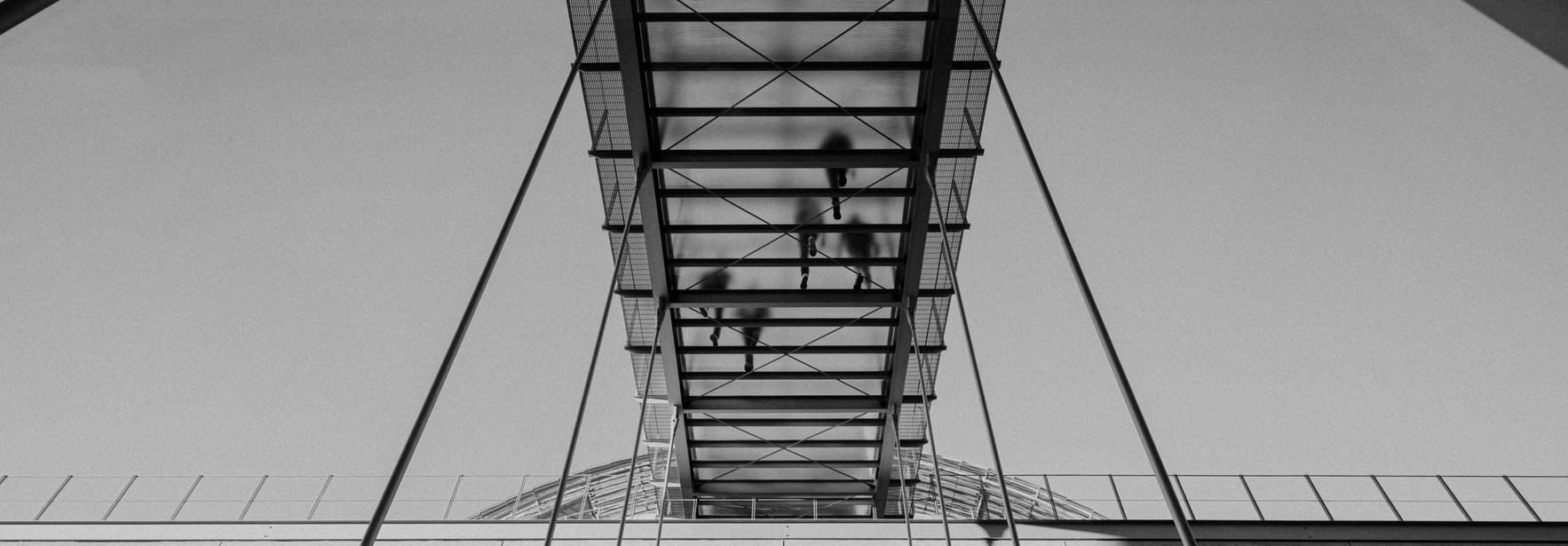 Una pasarela de vidrio suspendida sobre una estructura moderna con sombras proyectadas.