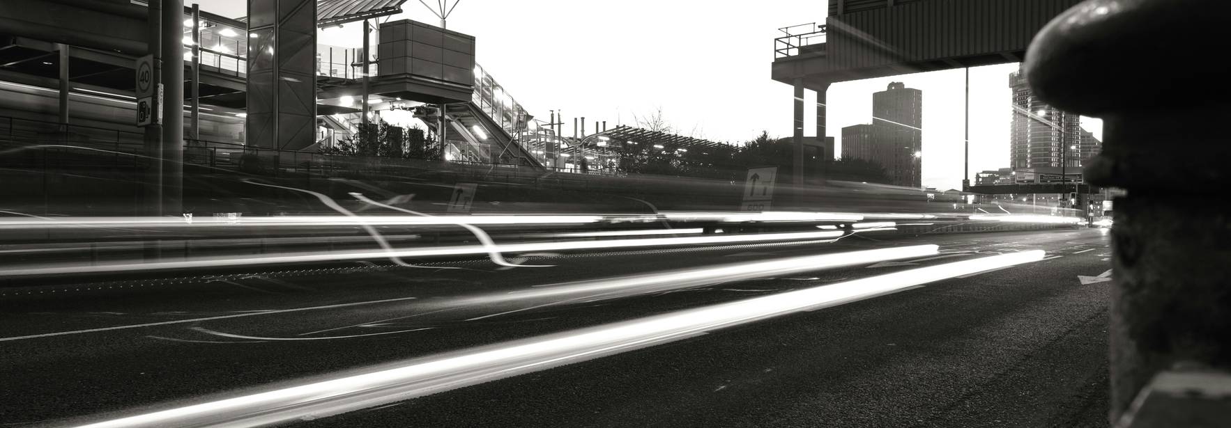 Una carretera iluminada por luces de vehículos en movimiento al atardecer, con una estructura moderna de fondo.