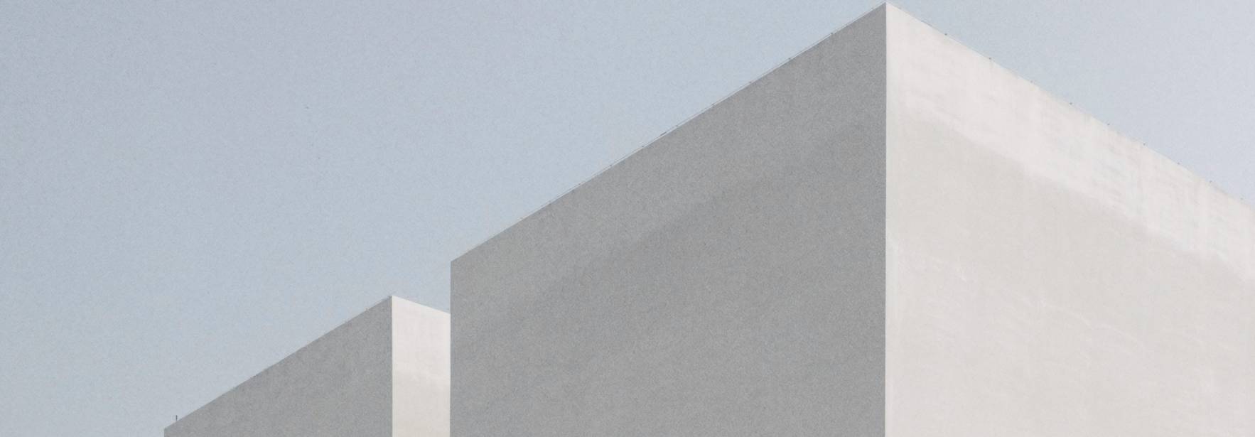 Edificios modernos de formas geométricas y colores neutros bajo un cielo claro.