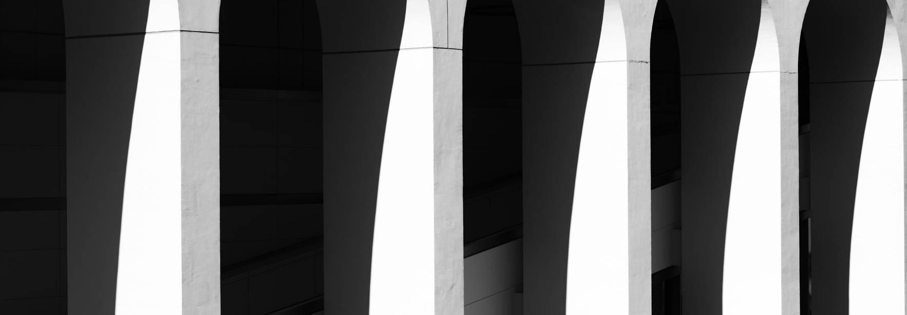 Una figura solitaria camina bajo columnas arquitectónicas en blanco y negro.