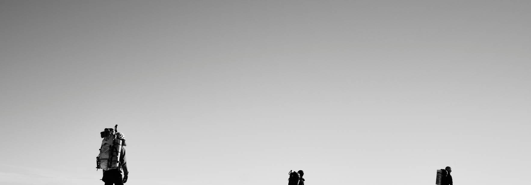 Un grupo de montañistas camina sobre un paisaje nevado en blanco y negro.