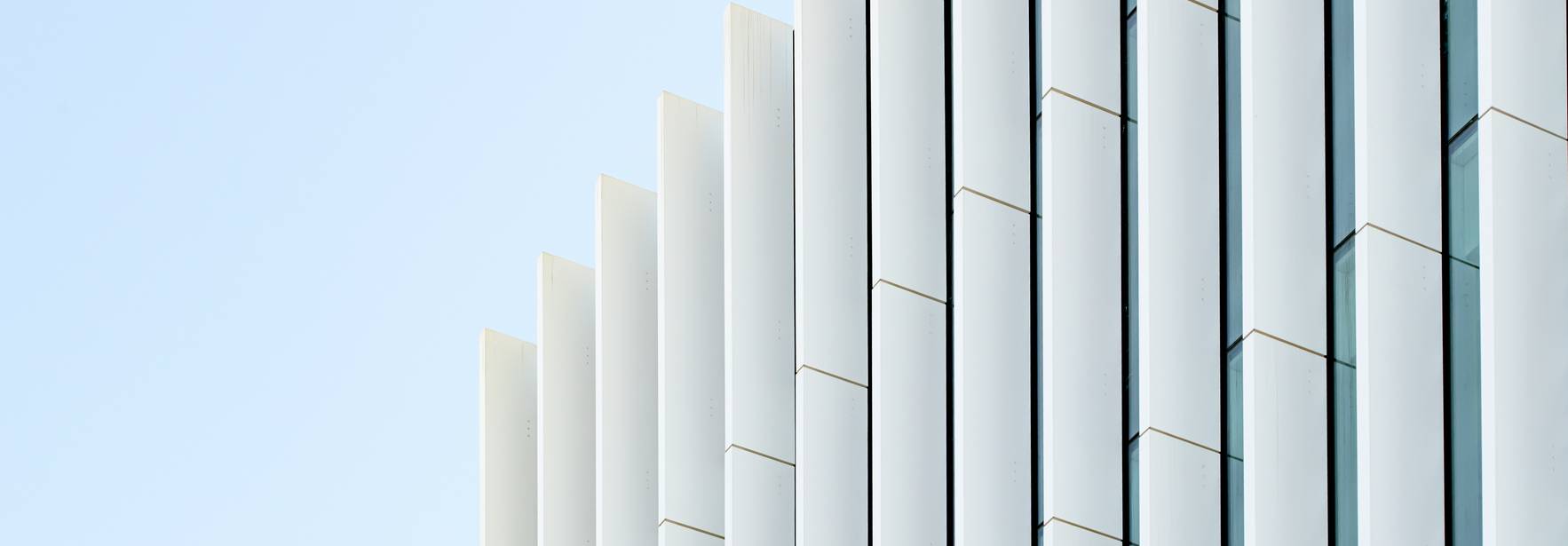 La imagen muestra un edificio modernista con una fachada de paneles blancos y líneas limpias.