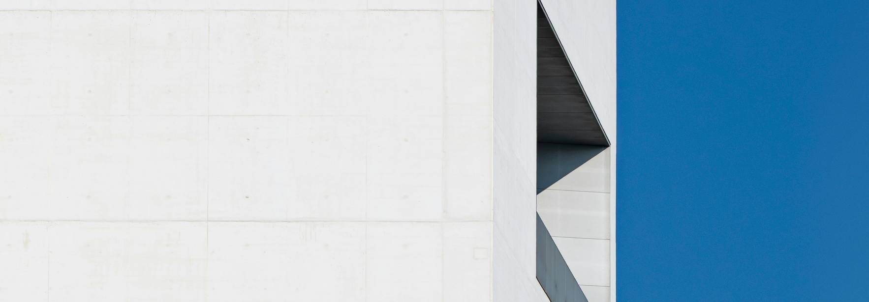 La imagen muestra una esquina de una estructura arquitectónica moderna con una ventana angular y un fondo azul claro.
