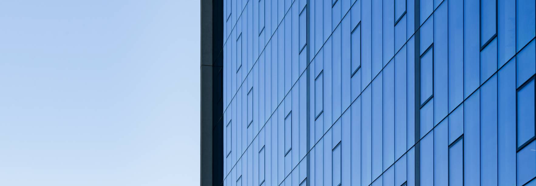 Una vista de un edificio moderno con una fachada de vidrio reflectante y un cielo claro al fondo.