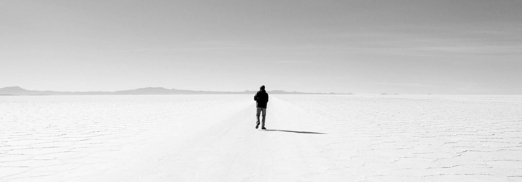 Una persona camina sola por un vasto paisaje desértico y blanquecino.