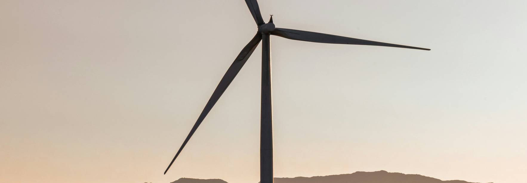Una turbina eólica se alza en un paisaje montañoso al atardecer.
