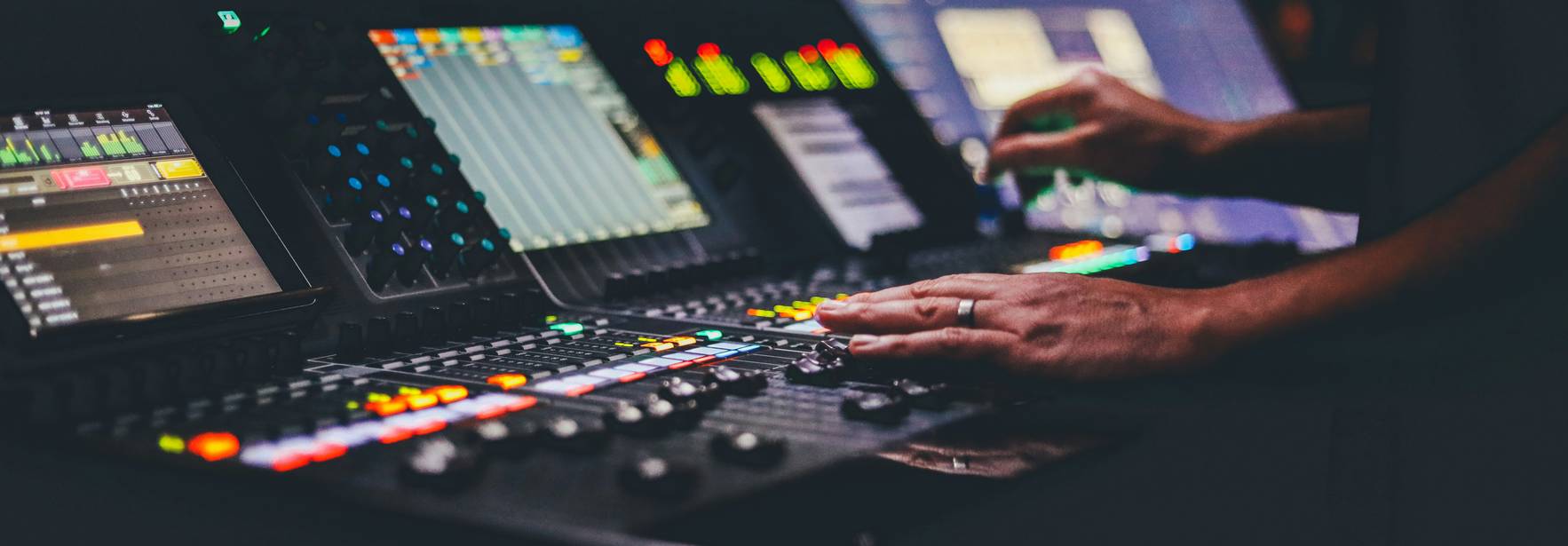 Una persona controla una consola de sonido con varios botones y pantallas iluminadas.