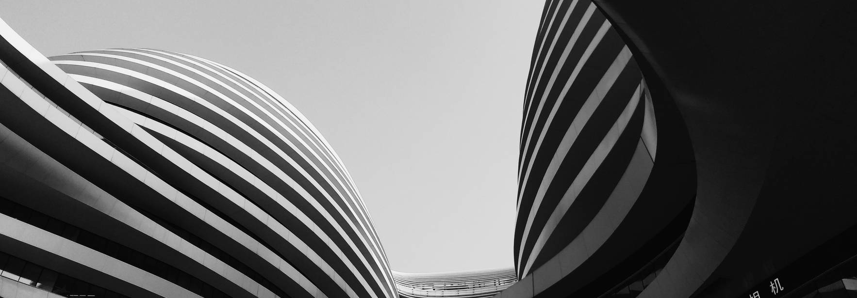 La imagen muestra una vista arquitectónica de edificios con formas curvas y líneas horizontales en blanco y negro.