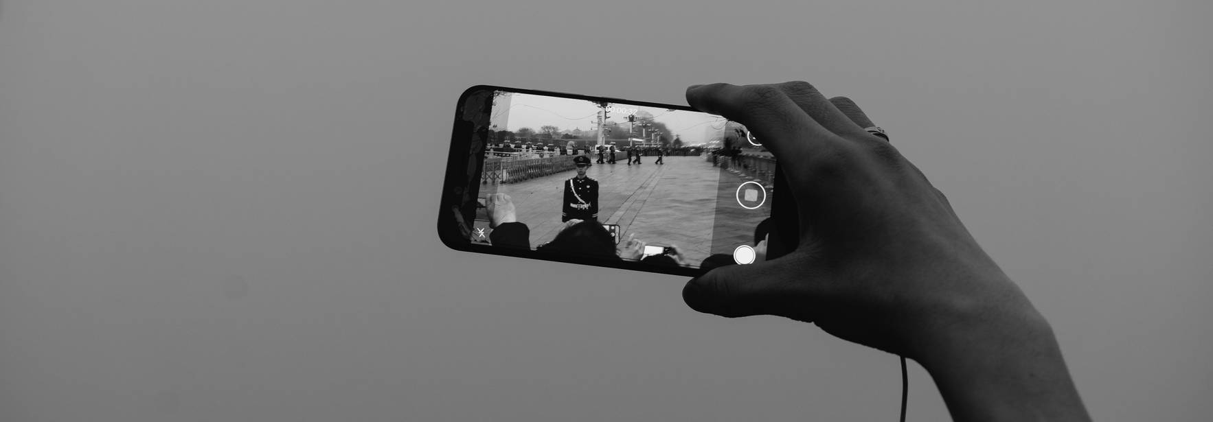 Una mano sostiene un teléfono móvil que captura una imagen de un evento al aire libre.
