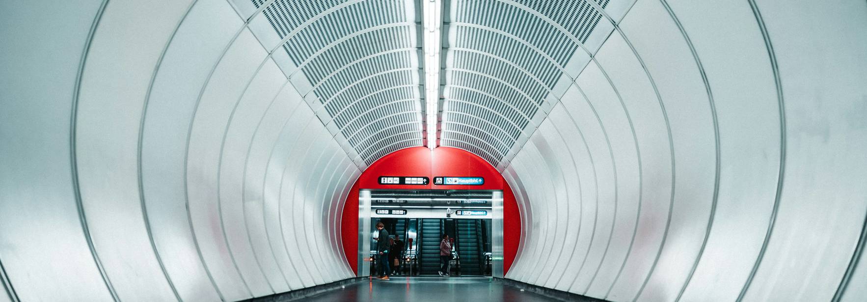 Un túnel moderno de estación de metro con iluminación blanca y paredes curvas de color plateado.