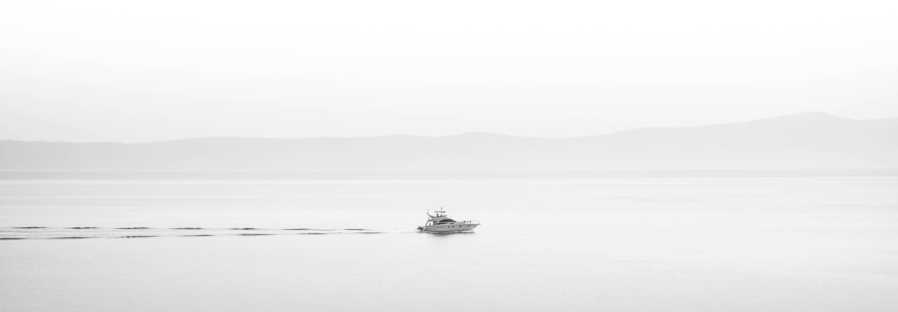 Un barco navega en un mar sereno y nebuloso.