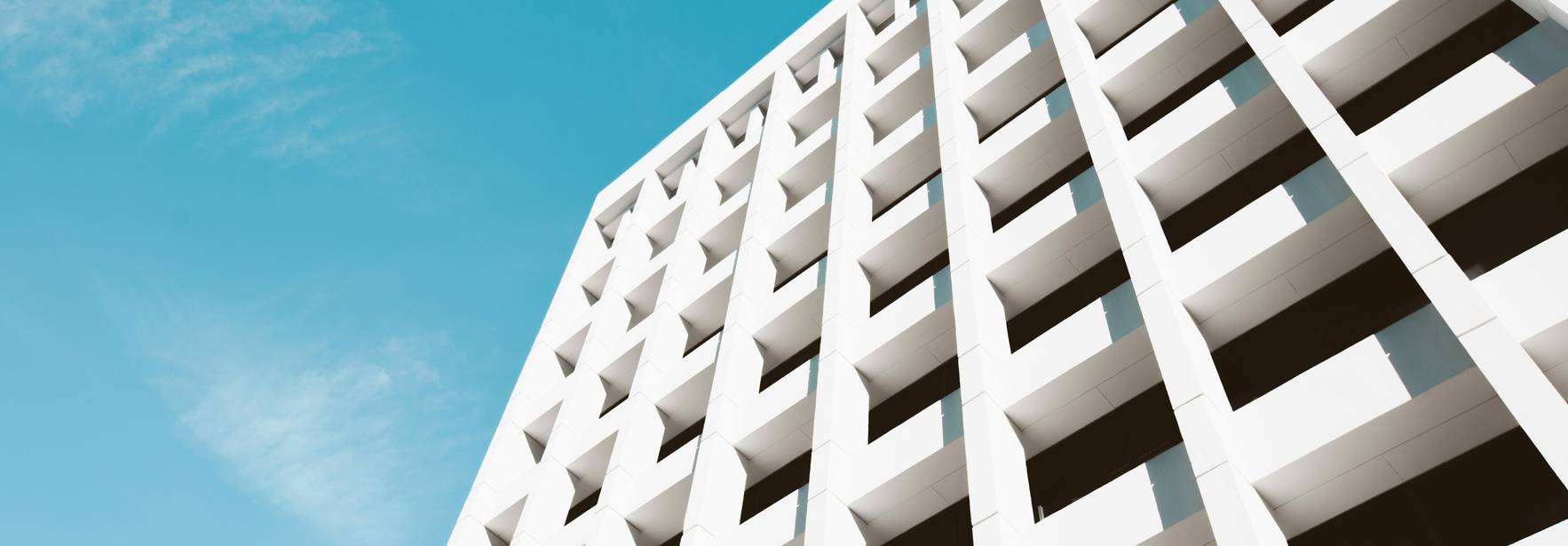 Una vista angular de un edificio moderno con una fachada de paneles blancos y un cielo azul claro.