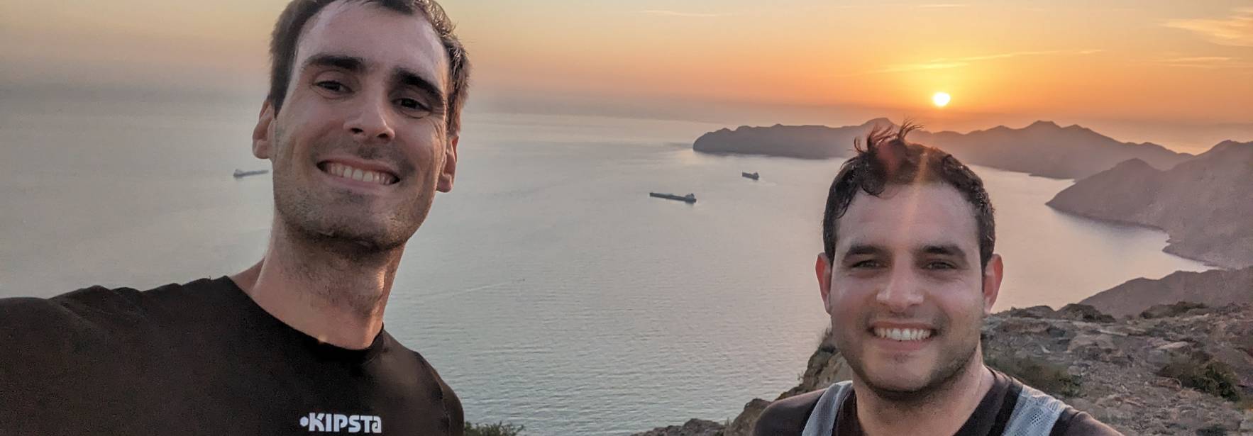 Dos amigos disfrutan de un atardecer en la cima de una montaña con vistas al mar.